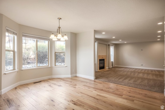 unfurnished living room with recessed lighting, a chandelier, light wood-style flooring, baseboards, and a tile fireplace