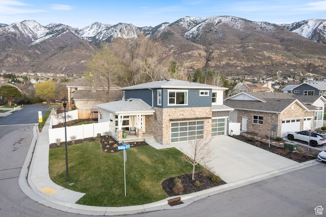 view of front of property featuring a mountain view, driveway, stone siding, a front lawn, and fence