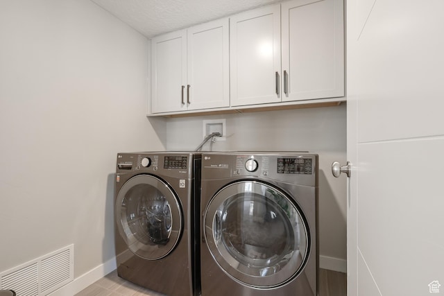 washroom with a textured ceiling, visible vents, baseboards, cabinet space, and washer and clothes dryer