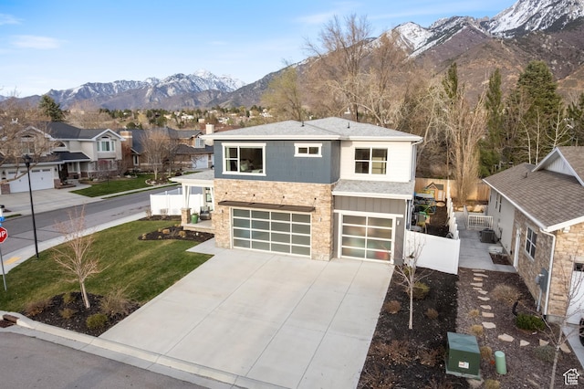 view of front of house with fence, stone siding, an attached garage, a mountain view, and driveway