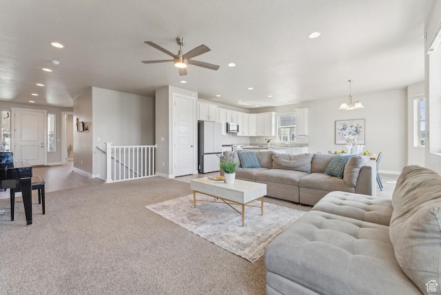 living area with light carpet, recessed lighting, ceiling fan with notable chandelier, and baseboards