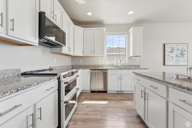 kitchen featuring white cabinets, dishwasher, a sink, light wood finished floors, and range with two ovens