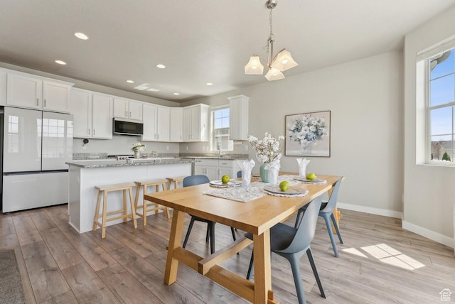 dining area featuring light wood-style flooring, recessed lighting, a notable chandelier, and baseboards