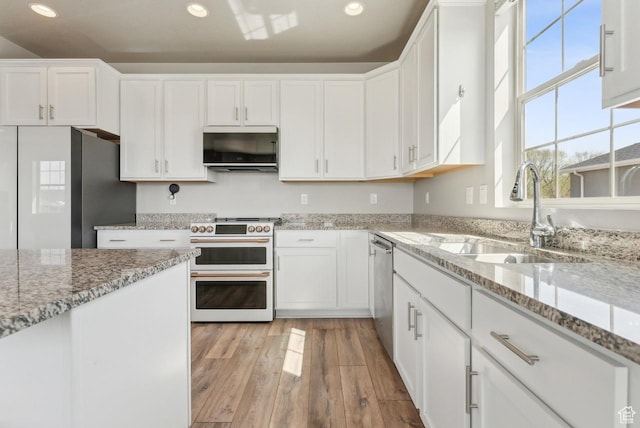 kitchen with stainless steel appliances, light wood finished floors, white cabinetry, and a sink