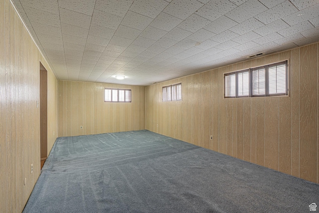 below grade area with carpet flooring, wooden walls, and visible vents