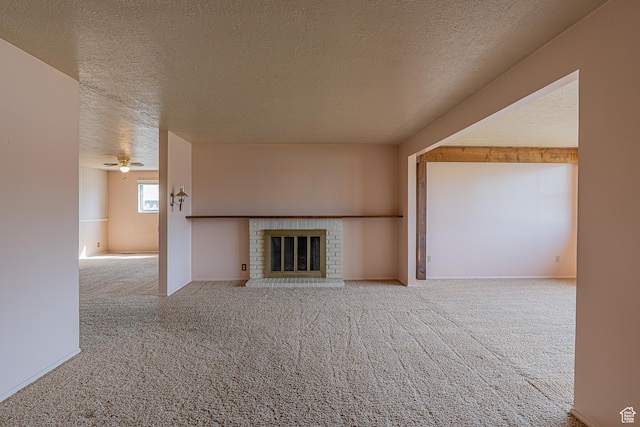 unfurnished living room featuring a textured ceiling, carpet flooring, ceiling fan, and a brick fireplace