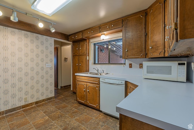 kitchen featuring white appliances, brown cabinetry, stone finish floor, a sink, and wallpapered walls