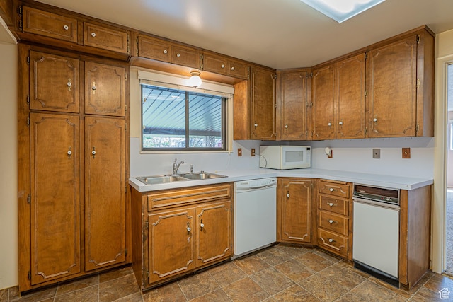kitchen with a sink, light countertops, white appliances, and brown cabinets