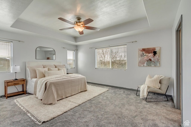carpeted bedroom featuring baseboards, a raised ceiling, and ceiling fan