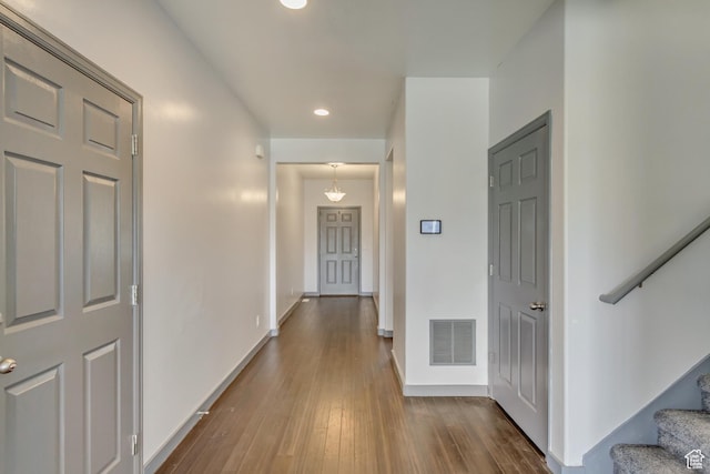 hallway with stairs, visible vents, baseboards, and wood finished floors