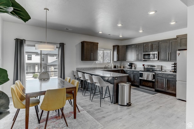 129 W Autumn Ln N, Saratoga Springs, UT 84045 - kitchen featuring appliances with stainless steel finishes, a peninsula, dark brown cabinets, light wood finished floors, and a sink
