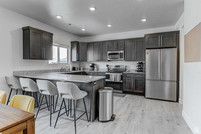 129 W Autumn Ln N, Saratoga Springs, UT 84045 - kitchen with appliances with stainless steel finishes, a peninsula, a sink, a breakfast bar area, and light wood-style floors