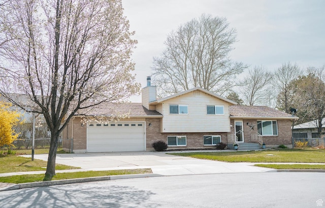 split level home featuring a garage, fence, brick siding, a chimney, and concrete driveway