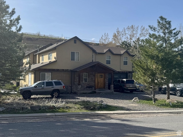 view of front of home featuring a garage, driveway, stucco siding, and stone siding