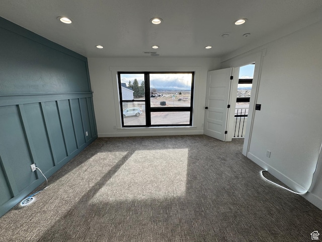 spare room with dark colored carpet, plenty of natural light, and recessed lighting