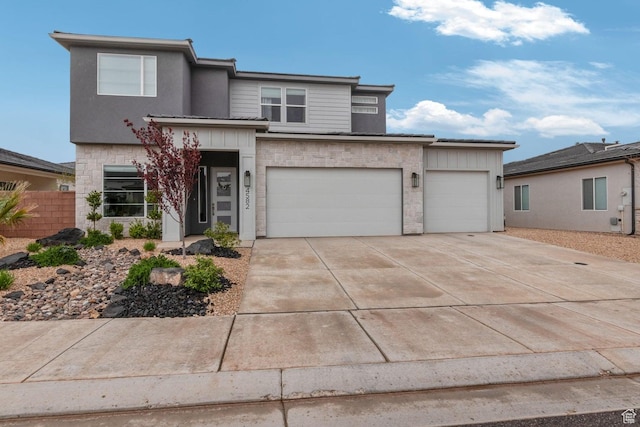 prairie-style home featuring concrete driveway, stone siding, board and batten siding, and fence