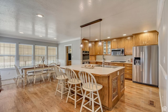kitchen with a sink, ornamental molding, light wood finished floors, and stainless steel appliances