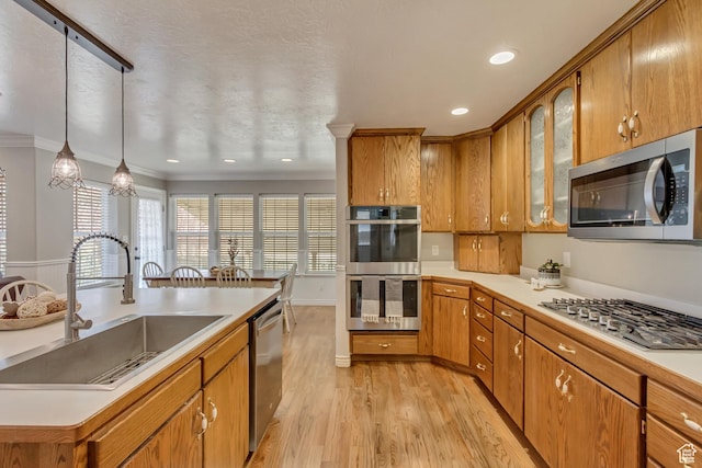 kitchen featuring a sink, light countertops, appliances with stainless steel finishes, brown cabinetry, and light wood finished floors
