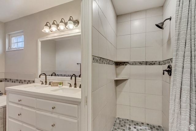 full bath with a sink, tiled shower, and double vanity