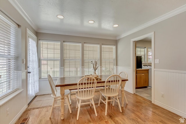 dining room with visible vents, ornamental molding, light wood-style flooring, and wainscoting