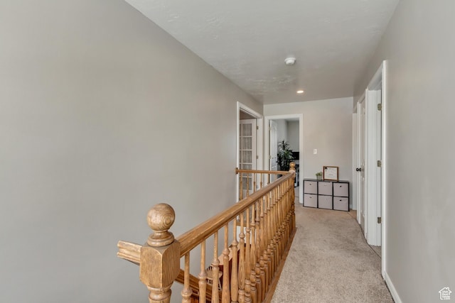 hall featuring baseboards, an upstairs landing, and light colored carpet