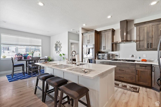 393 S Corner View Dr, Tooele, UT 84074 - kitchen with wall chimney range hood, a sink, appliances with stainless steel finishes, a breakfast bar area, and light wood-style flooring