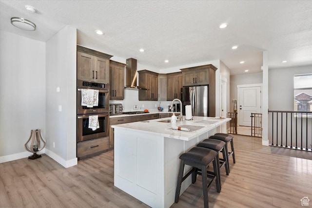 393 S Corner View Dr, Tooele, UT 84074 - kitchen with appliances with stainless steel finishes, wall chimney range hood, a sink, light wood finished floors, and a kitchen breakfast bar