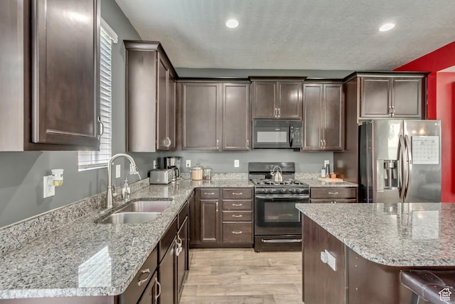 kitchen with a sink, black appliances, dark brown cabinetry, and light stone countertops