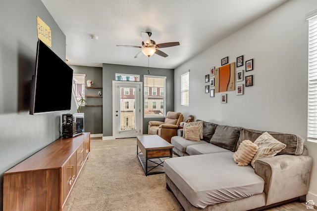 living area featuring light carpet, baseboards, and a ceiling fan