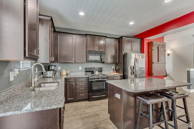 kitchen featuring a breakfast bar, a sink, black appliances, and dark brown cabinets