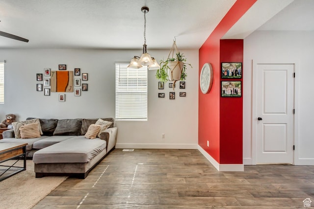 living area featuring wood finished floors, ceiling fan with notable chandelier, and baseboards