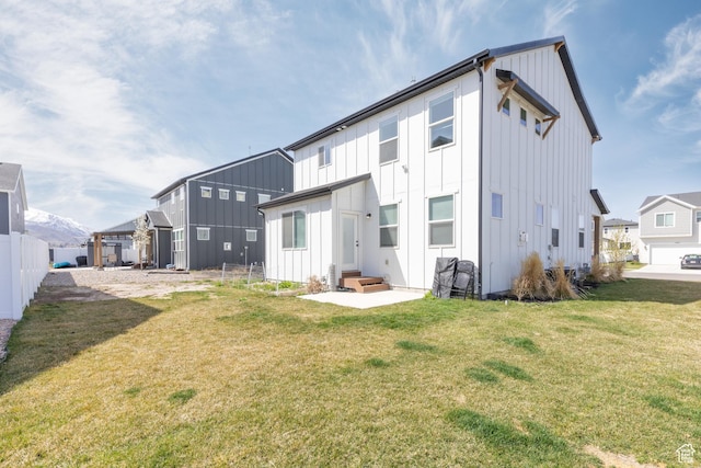 rear view of property featuring a yard, entry steps, board and batten siding, and fence
