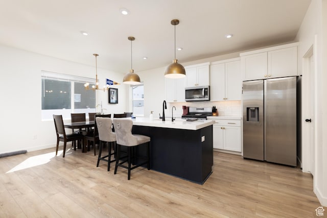 kitchen featuring light countertops, backsplash, white cabinetry, stainless steel appliances, and light wood finished floors
