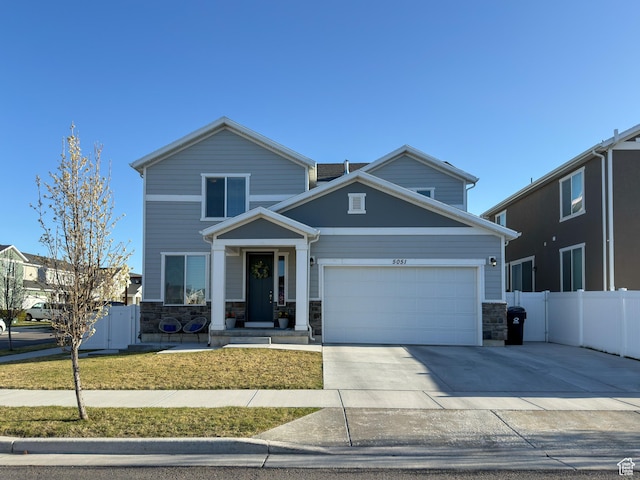 view of front facade featuring a garage, driveway, stone siding, and fence