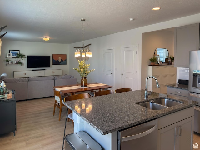 5051 W Bilston Ln S, Herriman, UT 84096 - kitchen featuring dark stone countertops, light wood-style flooring, a sink, a kitchen island with sink, and stainless steel dishwasher
