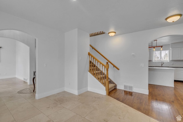 8079 S Juniper Ct, South Weber, UT 84405 - empty room featuring arched walkways, visible vents, a sink, stairs, and baseboards