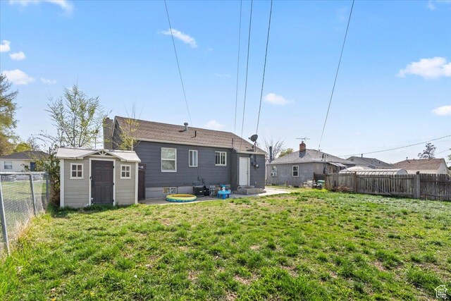 rear view of house with an outbuilding, a fenced backyard, a lawn, a patio, and a storage unit