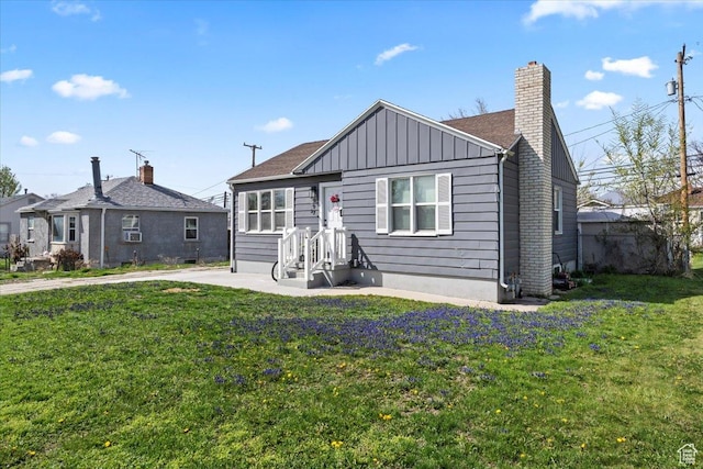 view of front facade featuring board and batten siding, a front yard, and a chimney