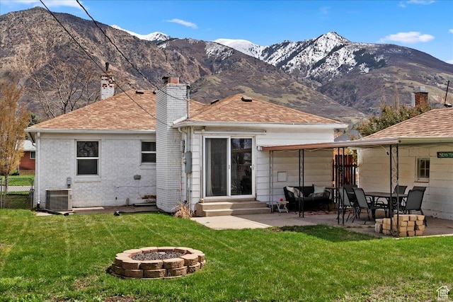 back of property with a mountain view, a fire pit, entry steps, a lawn, and a chimney