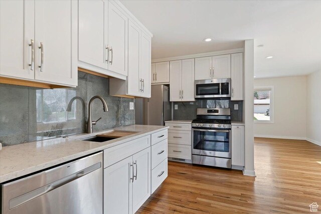 kitchen with stainless steel appliances, light wood-style floors, a sink, and backsplash