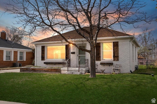 bungalow-style home featuring central air condition unit, fence, and a lawn