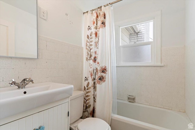 bathroom with shower / tub combo, tile walls, toilet, vanity, and a wainscoted wall
