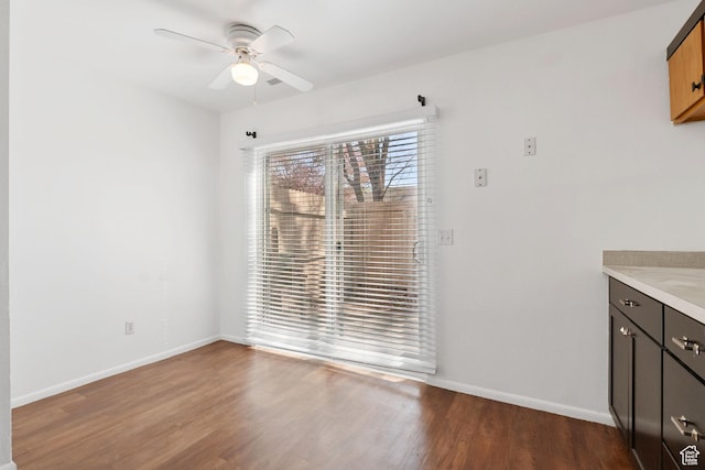 unfurnished dining area with ceiling fan, baseboards, and dark wood finished floors
