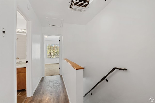 hall featuring baseboards, an upstairs landing, attic access, visible vents, and light wood finished floors