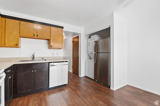 kitchen with a sink, light countertops, stacked washer and dryer, stainless steel appliances, and dark wood-type flooring