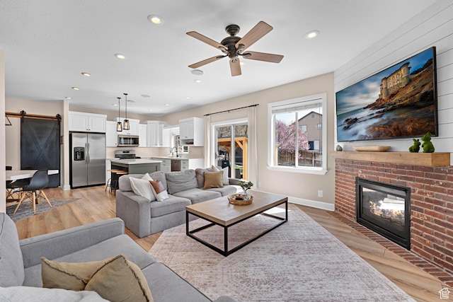 living room with light wood-style floors, ceiling fan, a fireplace, recessed lighting, and a barn door