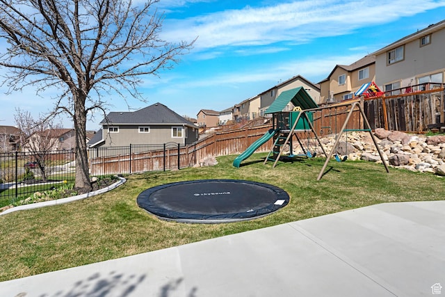 view of jungle gym featuring a yard, fence, a trampoline, and a residential view