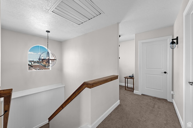 hall featuring a textured ceiling, carpet floors, a chandelier, an upstairs landing, and baseboards