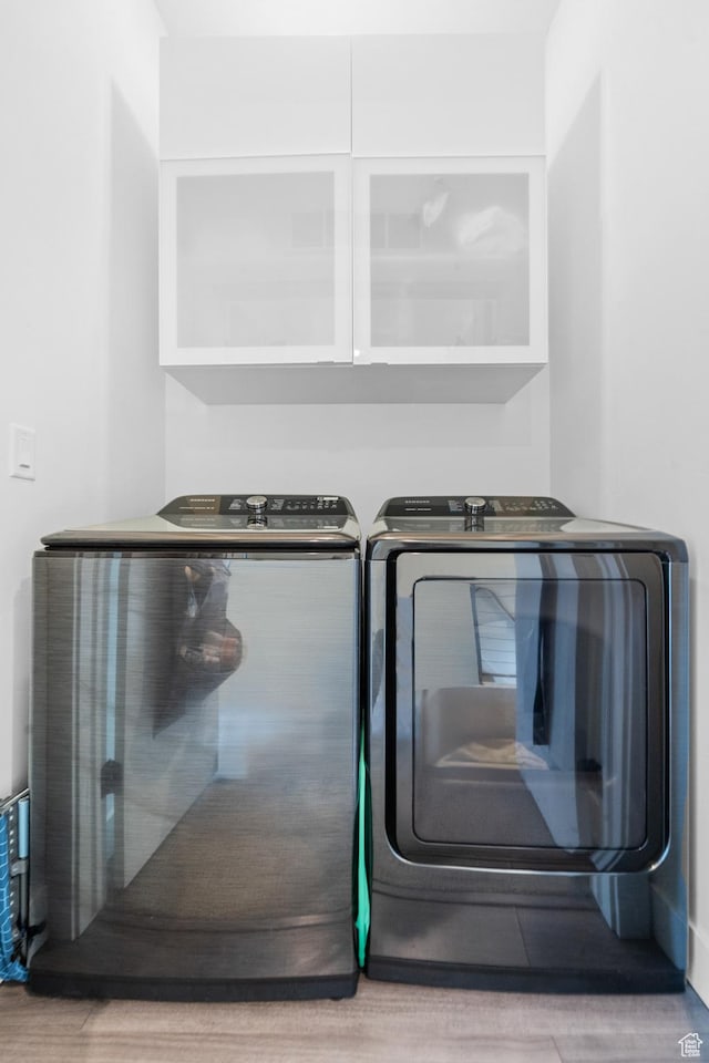 washroom featuring wood finished floors, cabinet space, and washer and clothes dryer