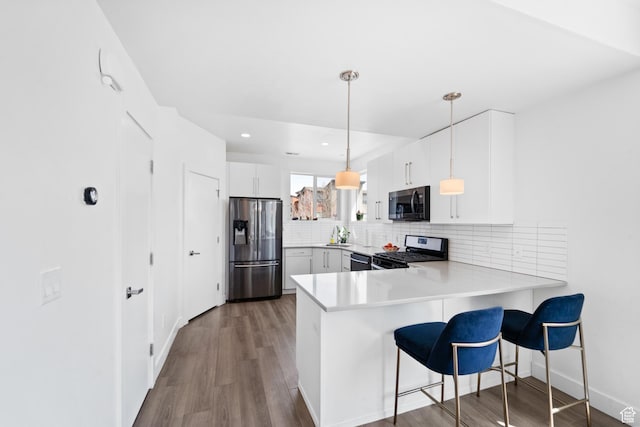 kitchen with a peninsula, light countertops, decorative backsplash, stainless steel appliances, and wood finished floors